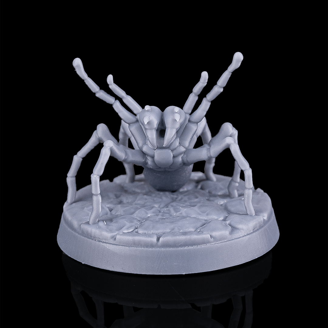 Gray spider-like figurine on a textured base against a black background