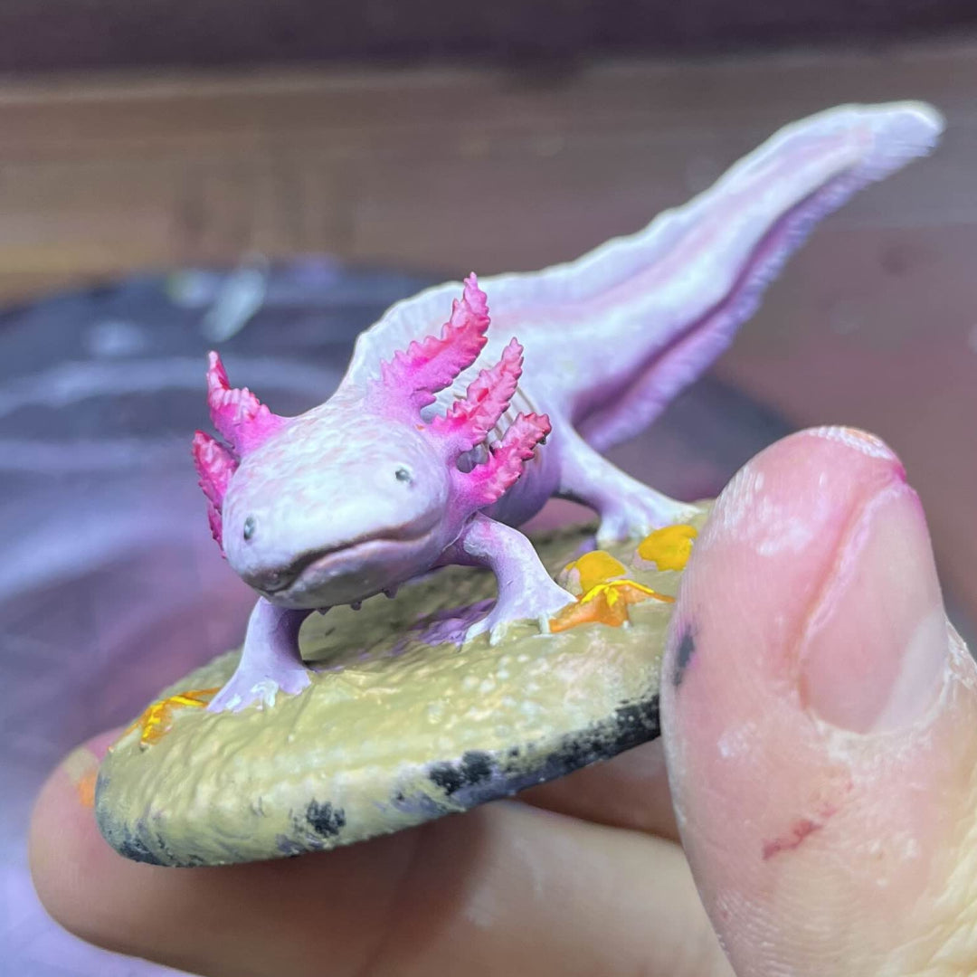 Small Painted Axolotl Familiar of a creature with pink accents held between fingers. This is for tabletop games like for D&D 5e play.