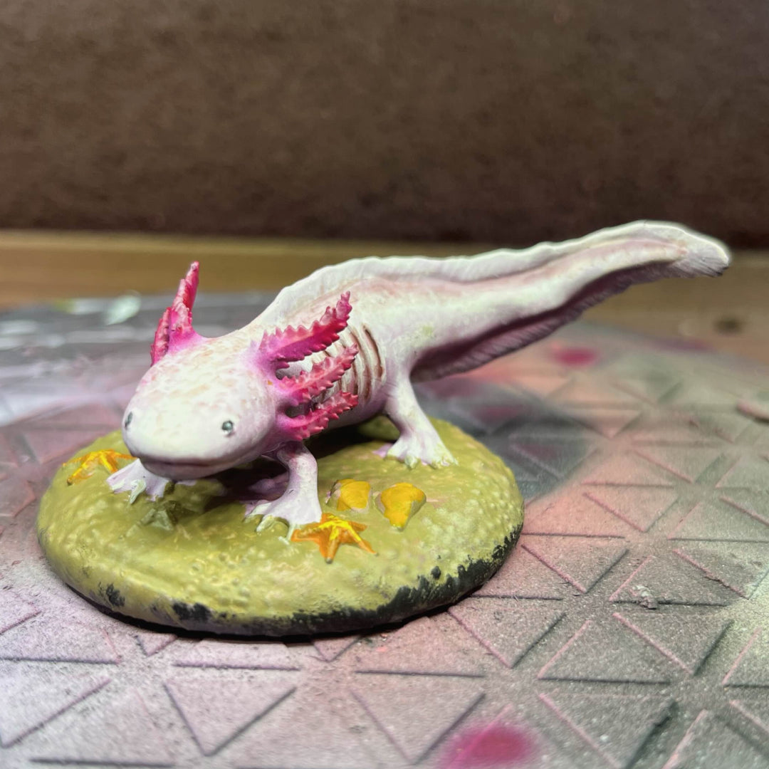 Painted model of a smiling axolotl on a beige base with a brown background. Front on view